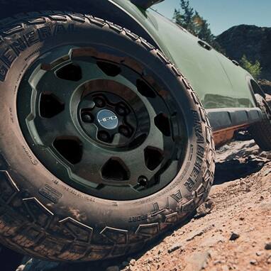 2027 Honda Passport TrailSport Elite in Ash Green Metallic profile on rocky terrain with black HPD wheels (Mid-Size SUV).