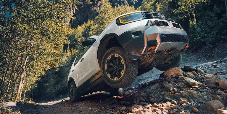 2027 Honda Passport TrailSport Elite in Platinum White Pearl front climbing a steep rocky mountain trail (Mid-Size SUV).